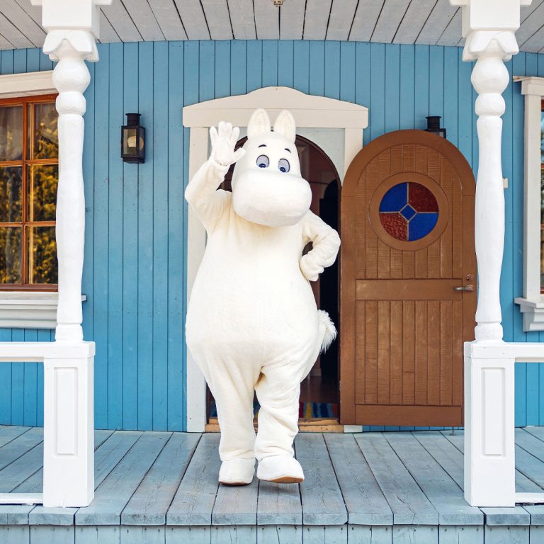 Muumipeikko vilkuttaa muumitalon kuistilla.