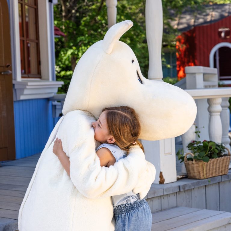 Muumipeikko ja tyttö halaavat Muumitalon edessä